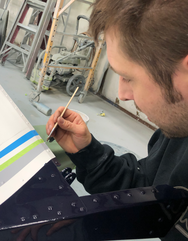 A paint technician meticulously paints the detail lines on an aircraft pinstripe.